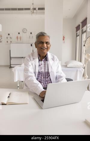 Portrait happy smiling older age doctor sitting at office workplace Stock Photo