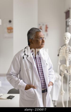 Thoughtful aged man doctor stand at workplace look at distance Stock Photo