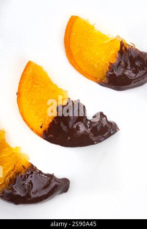 Three slices of candied oranges with dark chocolate dip. they are placed in a diagonal row on a white background Stock Photo