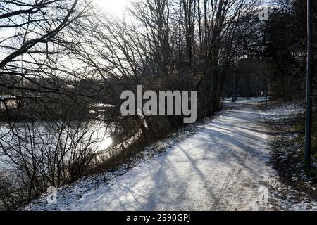 Lake shore in park with sun shining through tree branches Stock Photo