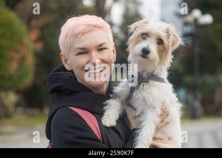 Attractive affectionate mature woman embracing pet dog Jack Russell Terrier in nature Stock Photo