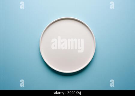 Top view of empty ceramic white plate on blue background Stock Photo