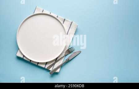 Top view of empty ceramic white plate and cutlery on blue background Stock Photo