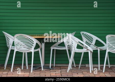 White plastic cafe chairs and a wooden table against a green panelled wall Stock Photo