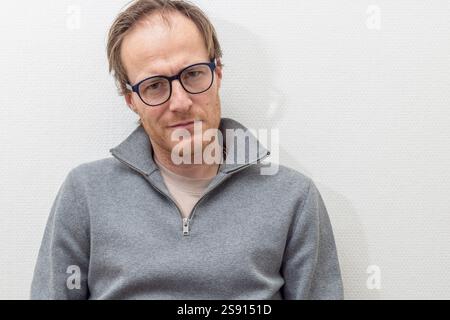 man with glasses leans against the wall while smiling softly Stock Photo