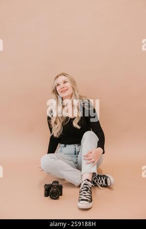 Young female photographer sitting with a camera on a beige background Stock Photo