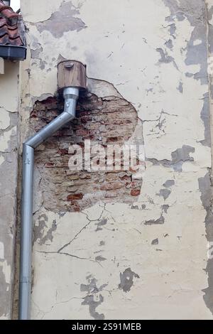 A fragment of the wall of an old building with decayed plaster exposing the brickwork and a system of rainwater drainage pipes attached to the wall. Stock Photo
