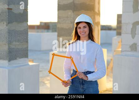 Confident female architect holding a folding ruler while inspecting a building under construction at sunset Stock Photo