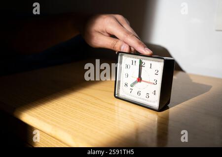Man reaching for his alarm clock after waking up in bed at home Stock Photo