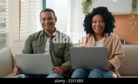 Multiracial couple in love working on laptops at home African American family business people work together on couch shopping online on computers Stock Photo