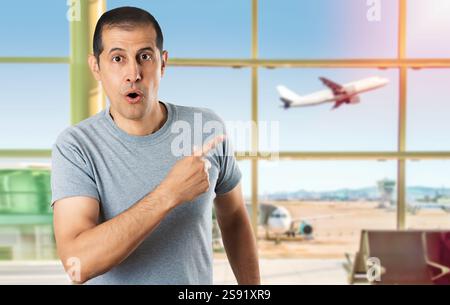 Handsome man wearing casual grey shirt at airport.Surprised pointing with finger to the side, open mouth amazed expression. Stock Photo