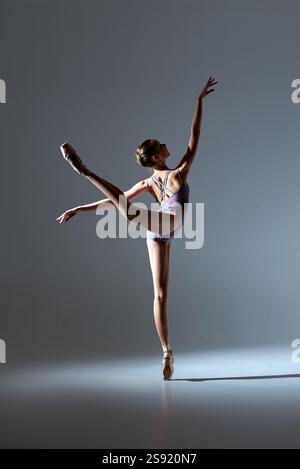 Stunning ballerina in a modern lavender leotard performing a dynamic arabesque on pointe. Beautiful studio light highlights her elegance and form. Stock Photo