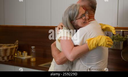 Mature wife dancing with middle-aged husband old retired couple in love having fun listen music funny dance together in kitchen washing dishes Stock Photo