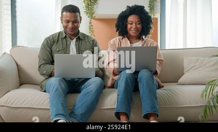 Multiracial couple African American Arabian family working laptops devices at home happy woman girlfriend and man boyfriend using computers gadget Stock Photo