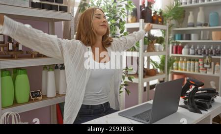 Young, attractive, hispanic woman stretching arms in a beautifully decorated home decor store, smiling happily surrounded by various products and gree Stock Photo