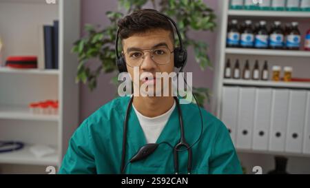 Young man in clinic wearing headset and glasses in a structured room with medical supplies and books visible on shelves behind, conveying a profession Stock Photo