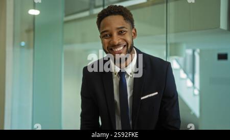 Young man in office wearing suit smiling against modern glass interior Stock Photo