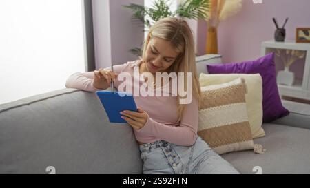 Woman sitting indoors in a comfortable living room, interacting with a tablet, showcasing a blend of modern technology and cozy home environment. Stock Photo