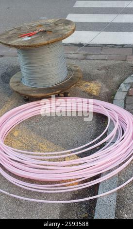 Pink fiber optic cable lying on the ground near a wooden spool with metal cable, suggesting telecommunications infrastructure work Stock Photo