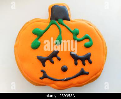 Close up of a smiling halloween pumpkin cookie decorated with orange, green and black icing, lying on a white surface Stock Photo