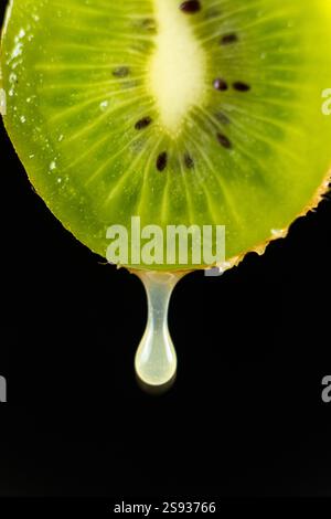 A drop of kiwi juice dripping from half a fresh kiwi fruit on a black background Stock Photo