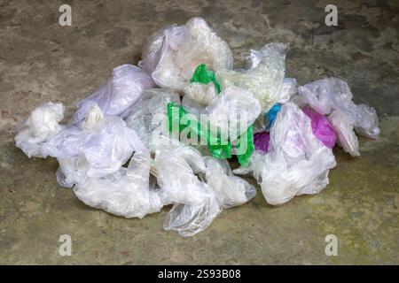 A pile of plastic bags in various colors on a cement floor. Designed for single-use convenience, plastic bags often contribute significantly to enviro Stock Photo