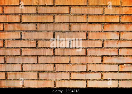 Textured brick wall with a consistent pattern of rectangular bricks arranged horizontally and vertically. The bricks are red light in color Stock Photo
