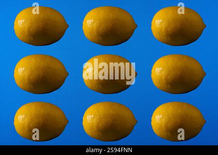 A seamless lemon pattern background with nine yellow lemons arranged in a grid on a vibrant blue surface. Ideal for use as a decorative or food-themed Stock Photo