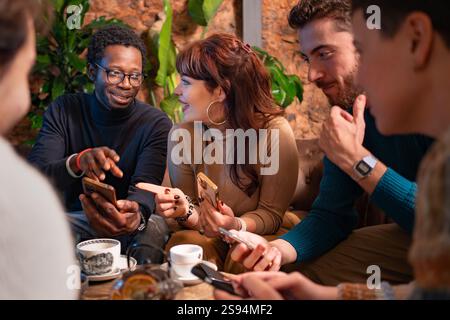 Group of multiracial friends enjoying a lively conversation and using smartphones at a cozy café. A warm and welcoming atmosphere emphasizing connecti Stock Photo