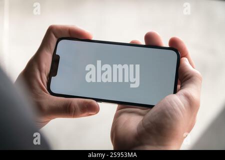 Close-up of a male hand swiping and tapping a mobile horizontally, with white screen. Stock Photo