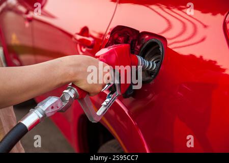 Selective focus view of the arm of a young man pumping gas into a red car Stock Photo