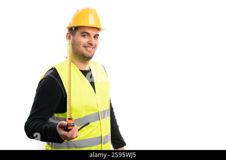 Friendly builder man wearing fluorescent vest and yellow safety hardhat smiling presenting tape measure with blank copyspace isolated on white Stock Photo