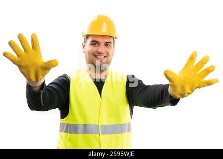 Smiling adult builder man wearing safety yellow hardhat and fluorescent vest showing hands with industrial trades work gloves isolated on white backgr Stock Photo