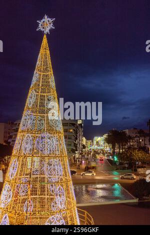 Vertical frame closeup of illuminated Christmas tree with glowing city lights seen from footbridge during blue hour sunset with San Pedro de Alcantara Stock Photo