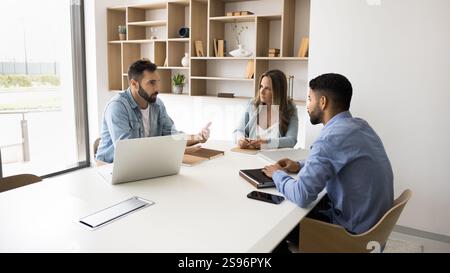 Three professionals sit at conference table engaged in discussion Stock Photo