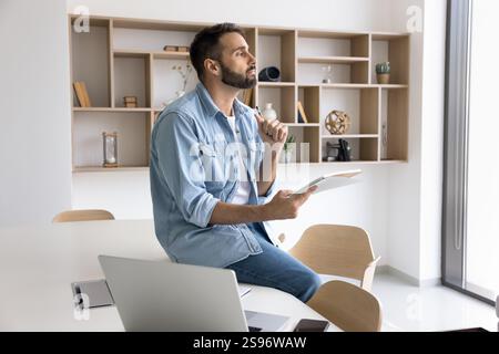 Pensive Hispanic employee working on creative ideas at modern workspace Stock Photo