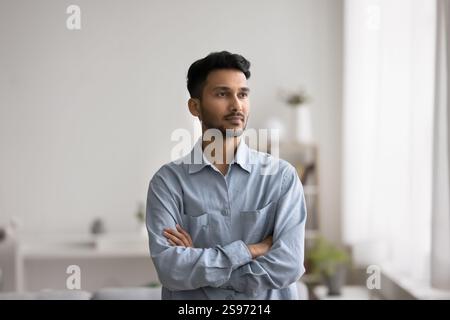 Confident thoughtful young man stand indoors thinking with arms crossed Stock Photo