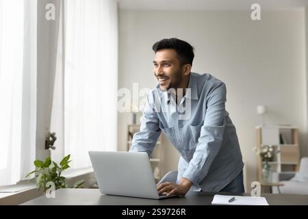 Smiling young man freelance worker stand by notebook look aside Stock Photo