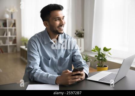 Smiling young man communicating on phone at workplace use notebook Stock Photo