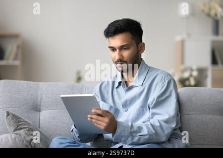 Focused young male freelancer working from home using digital tablet Stock Photo