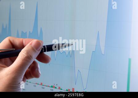 Man hand with pen pointing at financial stock graph on monitor screen, financial and trading concept. Stock Photo
