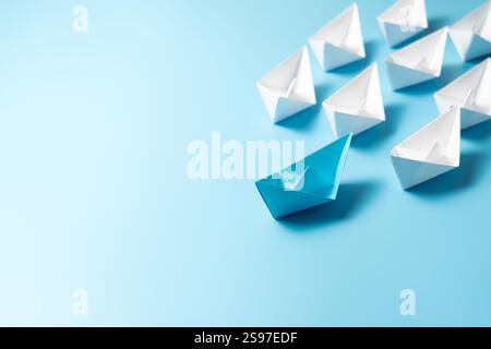 Leadership concept with blue paper ship leading among white boats isolated on blue background Stock Photo