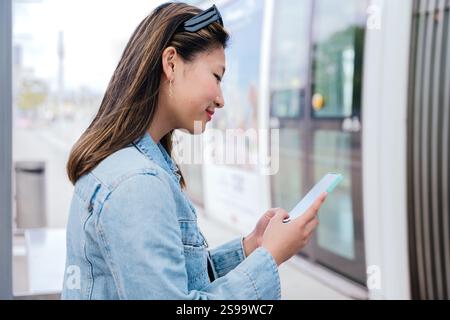 Young Woman Using Smartphone While Waiting for Tram to Board Stock Photo