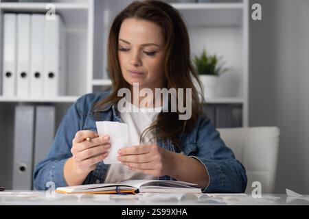 A woman is thoroughly analyzing various receipts in a contemporary office environment, demonstrating her professional skills and focus on details Stock Photo