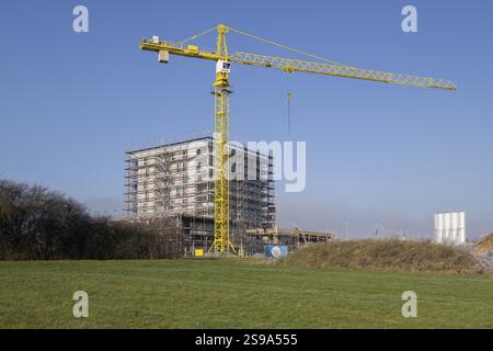 Building under construction behind overgrown hill, with crane and clear sky, residential construction, new construction of 50 flats, new development a Stock Photo
