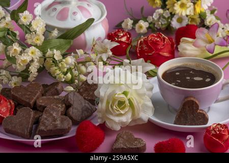 Coffee mug with heart-shaped chocolate and roses on a pink background, Valentine's Day Stock Photo