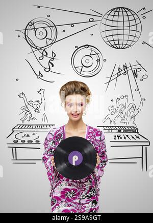 Colourful photo of a clubbing fashionable hippie deejay at the dance party holding a retro vinyl record in his hands on a grey sketchy background of a Stock Photo