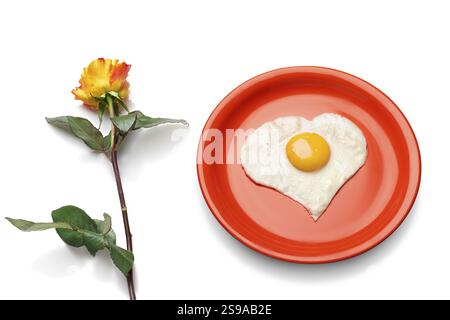 Heart-shaped egg on the red plate next to a fresh rose Stock Photo