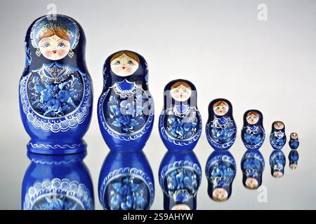 A set of seven blue-painted Russian nesting dolls on a mirror surface Stock Photo