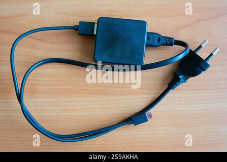 Black charger with a detachable cable lies on a wooden surface. This device is commonly used for charging various electronic gadgets efficiently. Stock Photo